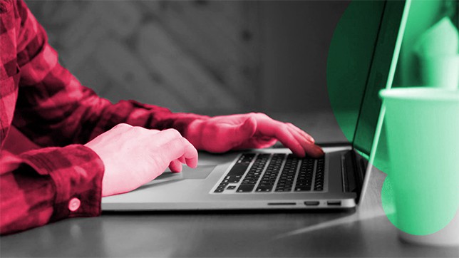 Mains sur un clavier d'ordinateur portable, chemise framboise et gobelet menthe